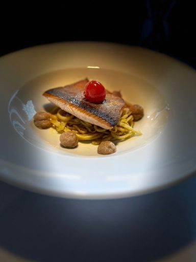 Gerösteter Fischfilet auf Nudeln, garniert mit Kirschtomate und Nüssen.