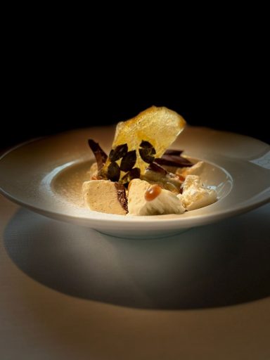 Feine Speise mit cremiger Sauce, knusprigen Chips und dekorativen Kräutern.
