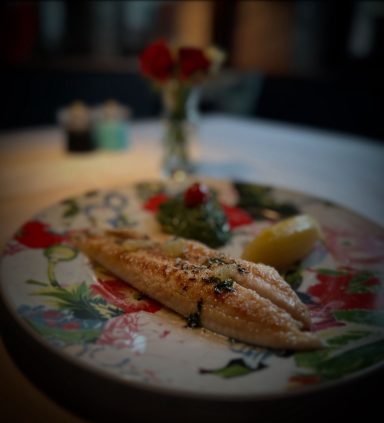 Gegrillter Fischfilet mit Beilagen und einem Zitronenstück, dekoriert mit Kräutern.