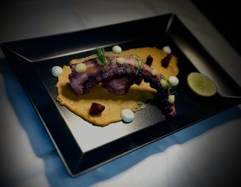 Gegrillter Oktopus auf püriertem Gemüse mit Limettenscheibe und Garnitur.