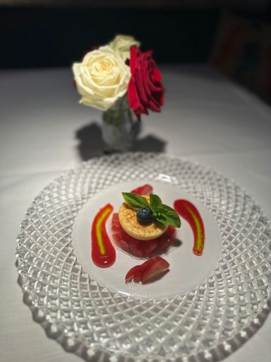 Dessert mit Beeren, frischer Minze und dekorativen Saucen auf einem eleganten Teller.