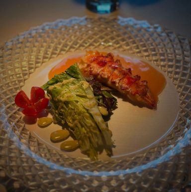 Ein kunstvoll angerichteter Teller mit gegrilltem Fisch, Salat und Soße.